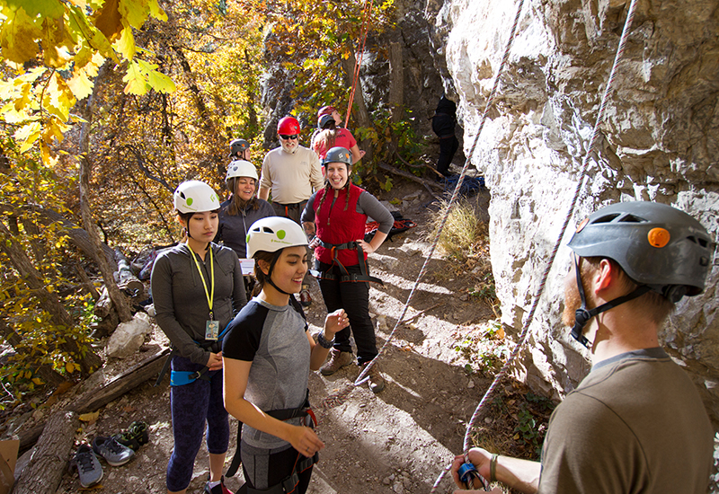 People stand at the bottom of a cliff prepared to begin rock climbing.