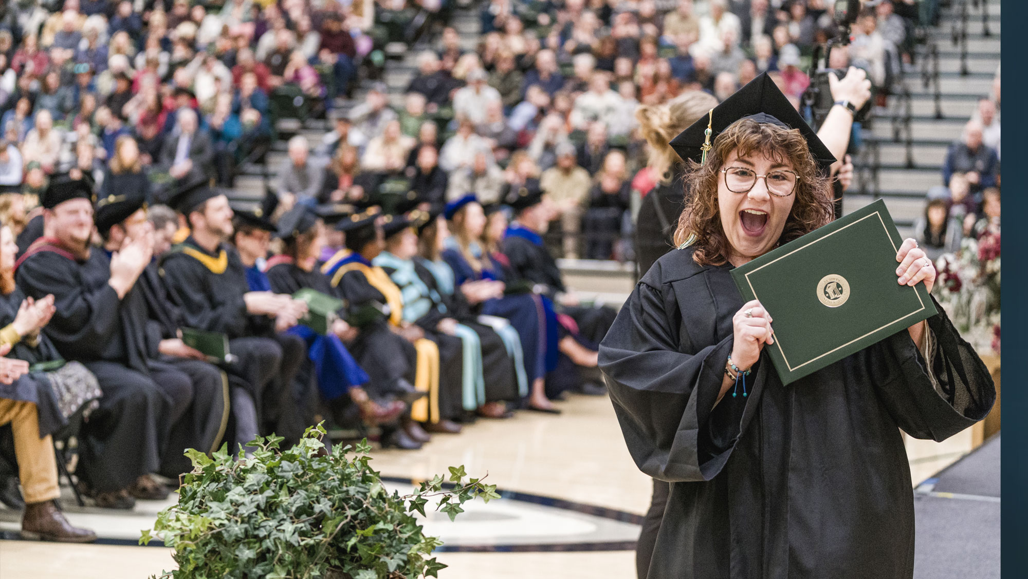 BHSU graduate poses smiling with degree at a commencement ceremony